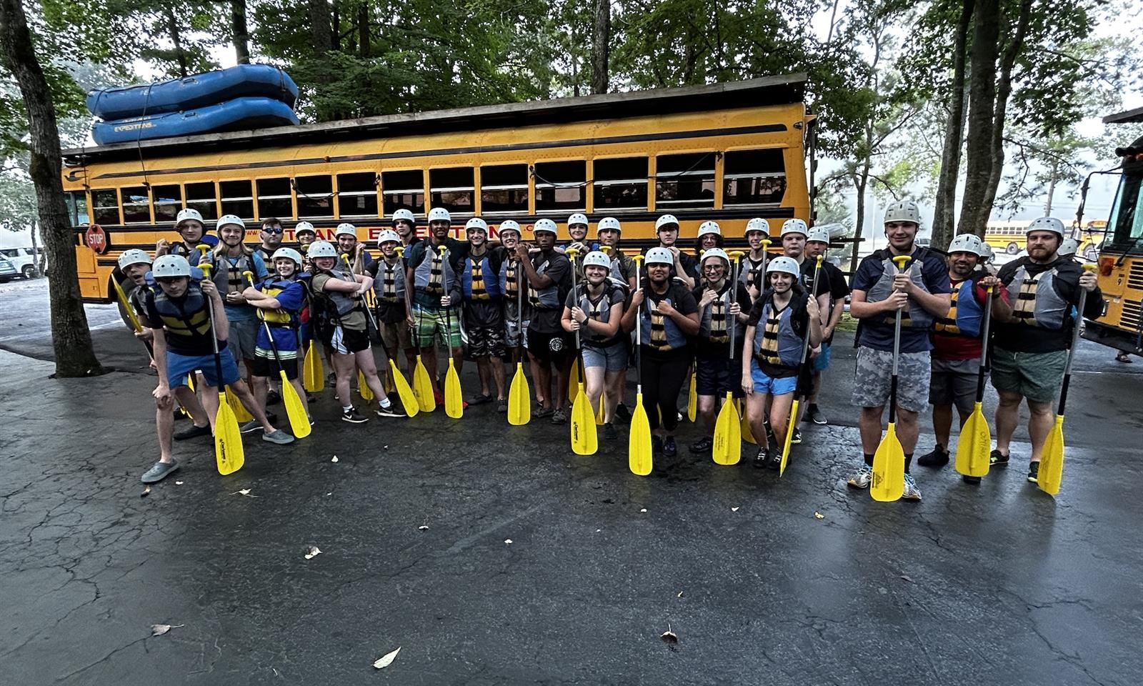 JROTC students stand with rafting oars in front of a school bus